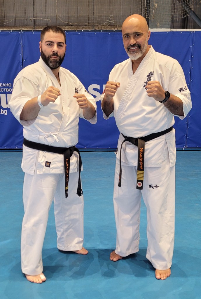 Two Kyokushin black belt instructors posing together in fighting stances against a blue background.