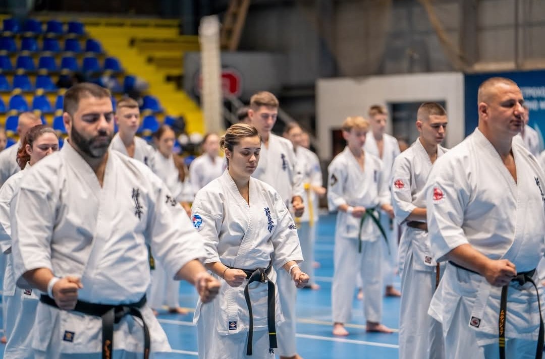A row of karate practitioners standing in a meditative "Mokuso" or formal ready stance with eyes closed and fists clenched.